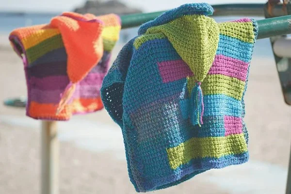 Two brightly coloured, hooded crochet kids ponchos.