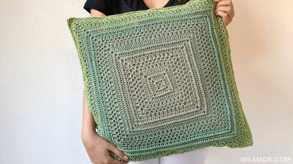 A large textured granny square pillow in green gradient yarn.