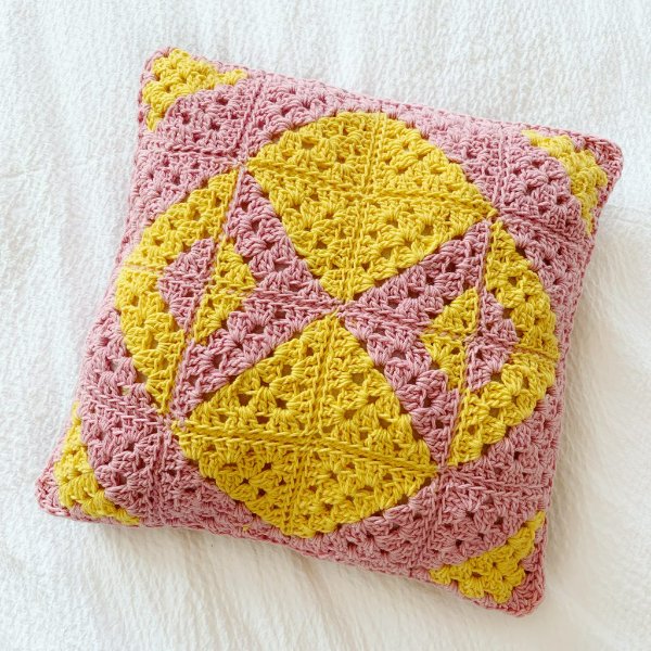 A pink and mustard yellow geometric patterned crochet granny square pillow.