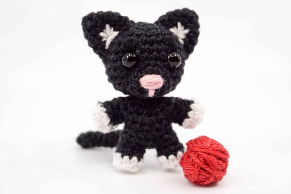 A mini crochet cat with a red yarn ball.