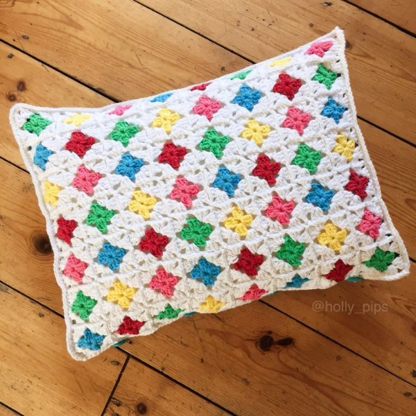 A rectangular crochet granny square cushion with rainbow colours.
