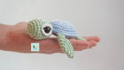 A pastel-coloured amigurumi sea turtle in the palm of a hand.