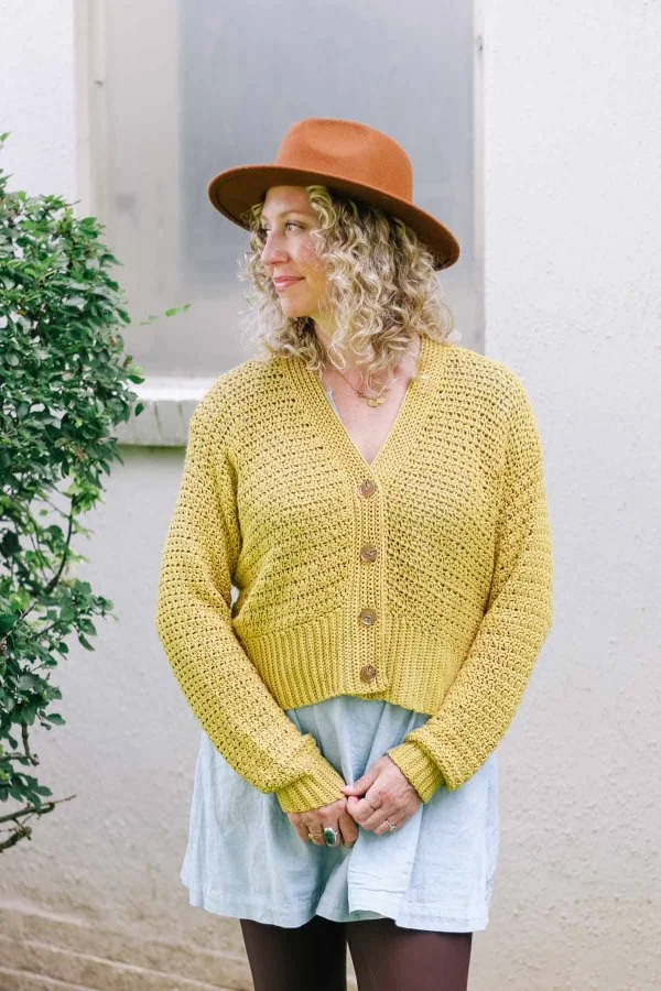 A woman wearing a yeloow, button-up cropped crochet cardigan.