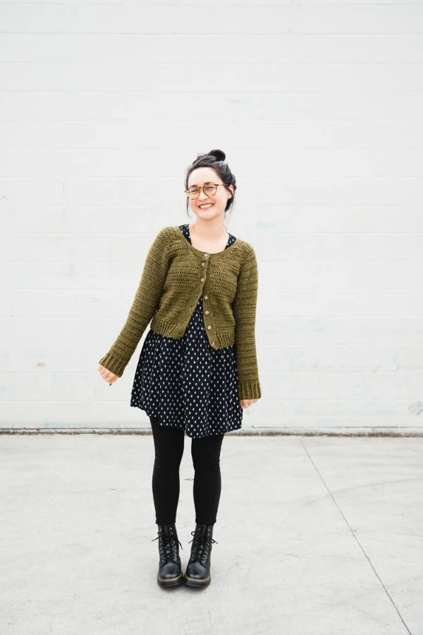 A young woman wearing a modern, cropped crochet cardigan with a dress and tights.