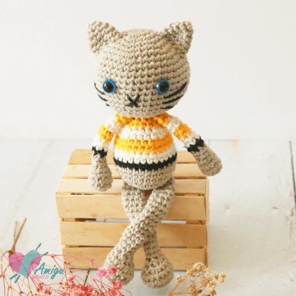 A crochet cat sitting on a timber box weraing a striped sweater.