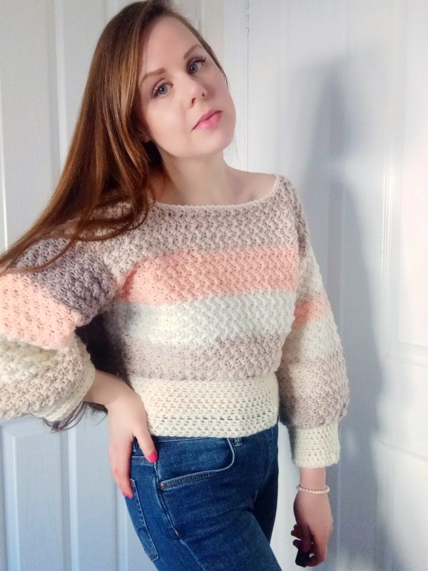 A woman wearing a striped crochet cropped sweater with jeans.