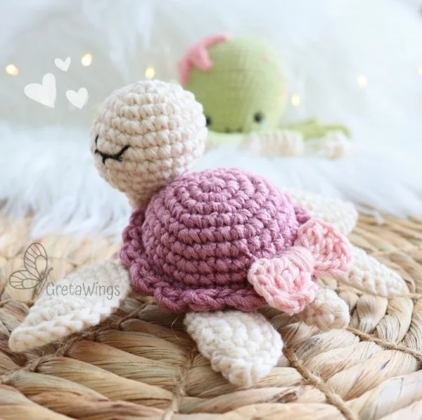A pink crochet turtle with a pink bow on it's shell.