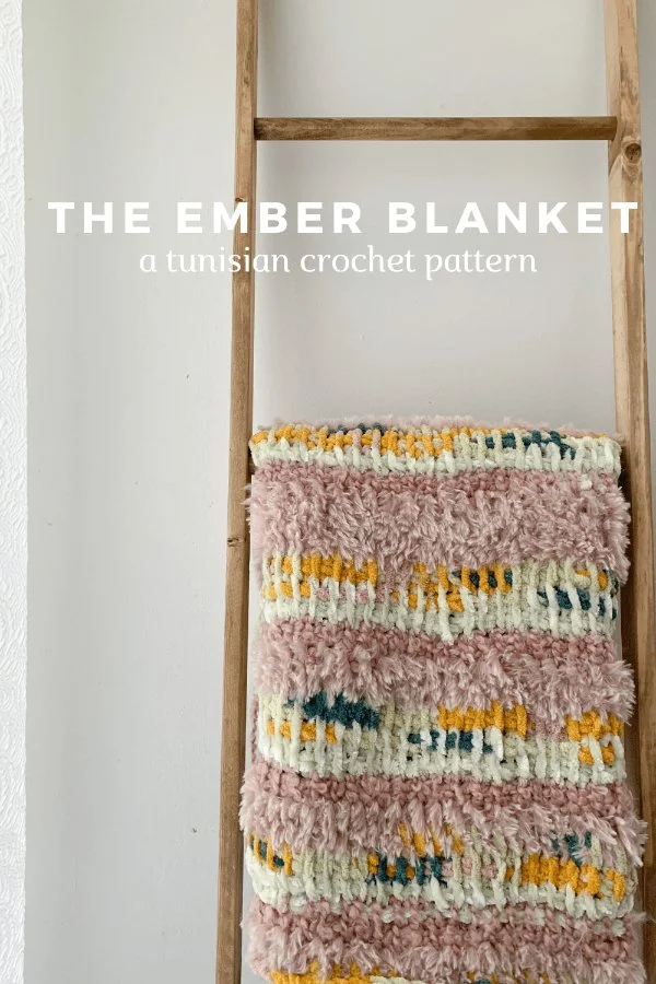 A textured, chunky crochet blanket hanging on a ladder.