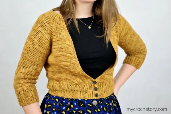 Close up of a woman wearring a mustard yellow cropped crochet cardigan with buttons.