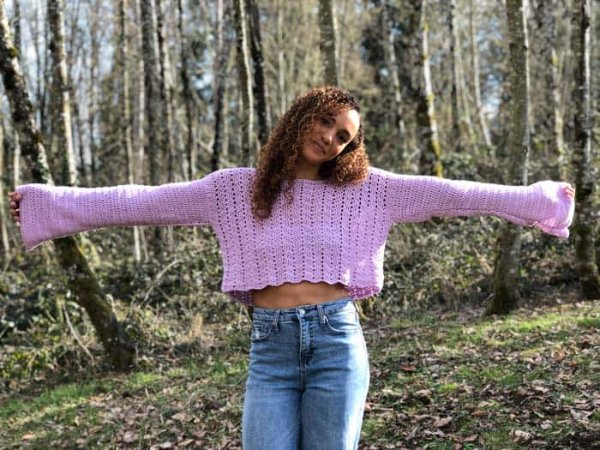 A woman outdoors weatring a lavender cropped crochet sweater and jeans.