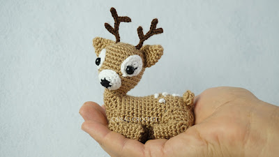 A crochet deer sitting in the palm of a hand.