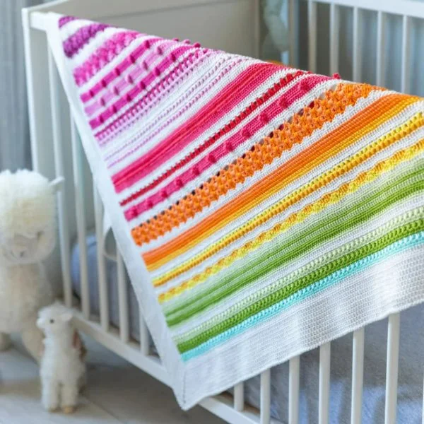 A crochet sampler baby blanket in rainbow colours.