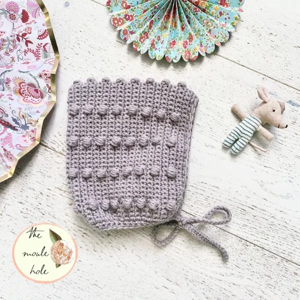 A mauve-coloured crochet baby bonnet.