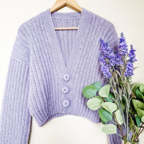 A lavender crochet button-up cardigan on a wooden clothes hanger.