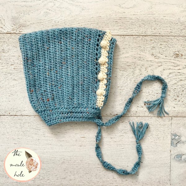 A blue crochet bonnet with contrasting bobble stitch edging.