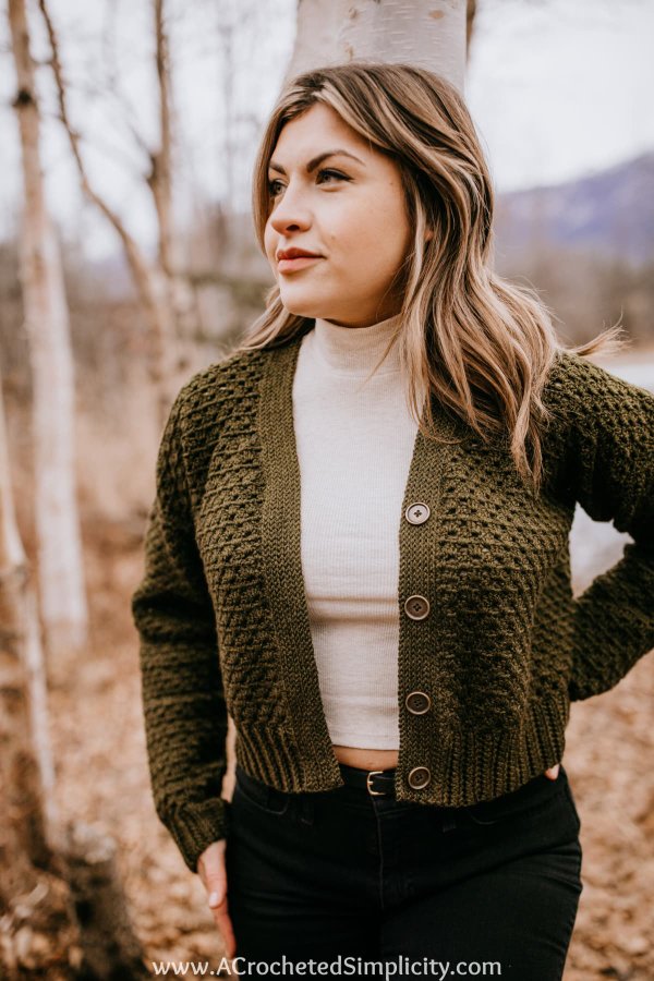 A woman wearing an olive green crochet button-up cardigan over a white tee.