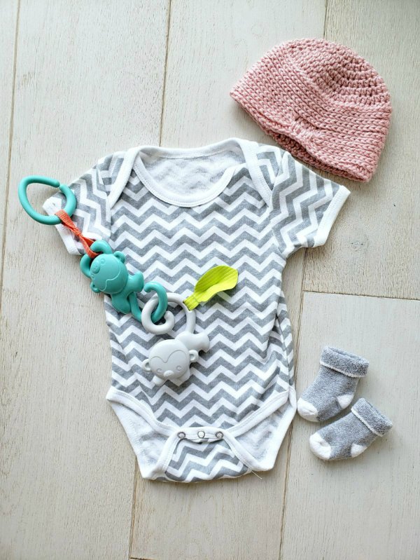 A flat lay image of a pink crochet baby turban with a onesie and booties.