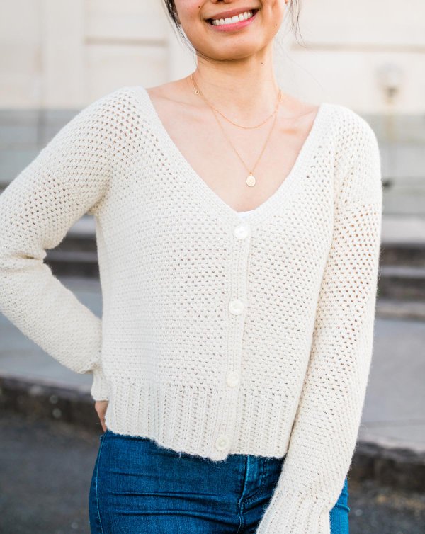 A close-up image of a woman wearing a white button down crochet cardigan.