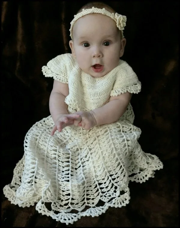 A bab -y wearing a crochet christening gown and a crochet headband.