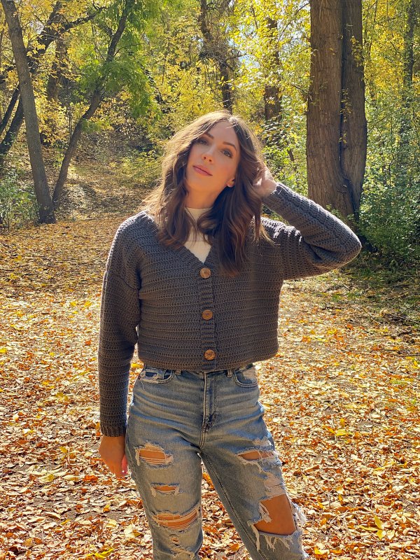 A woman wearing a button-up crochet cardigan with torn jeans.