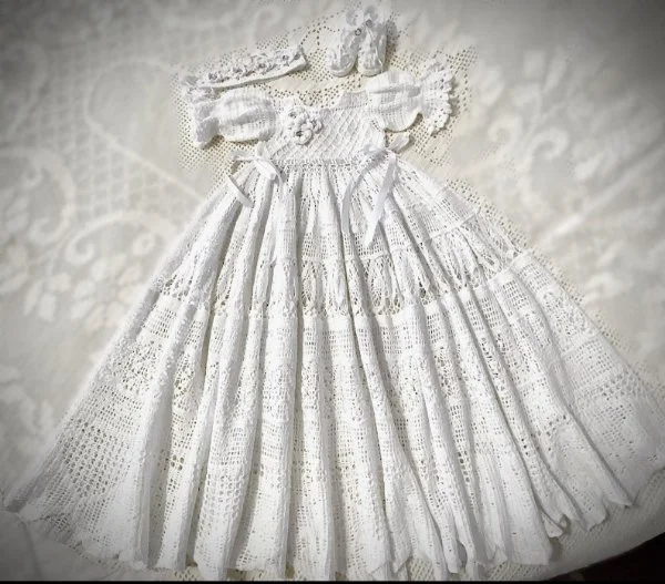 A flat lay image of a white crochet christening dress featuring filet crochet lace.