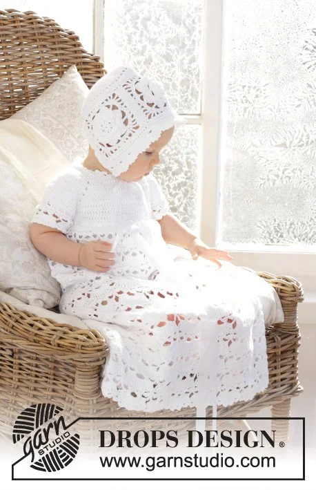 A baby sitting in a wicker chair, dressed in a crochet bonnet and lacy crochet christening gown.