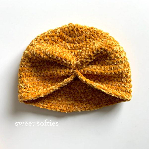 A crochet baby turban made in yellow velvet yarn.