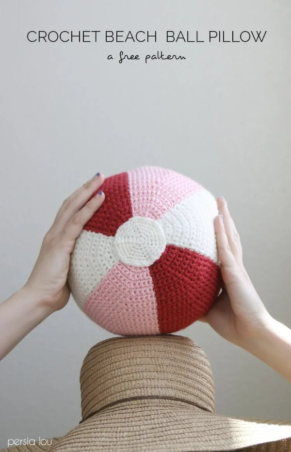 A close-up image of a person holding a pink crochet beach ball above their head.