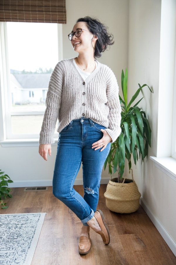 A woman wearing jeans and a crochet button-up cardigan sweater.