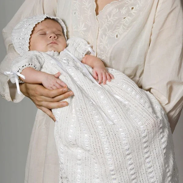 A woman holding a baby dressed i a crochet christening dress and bonnet.