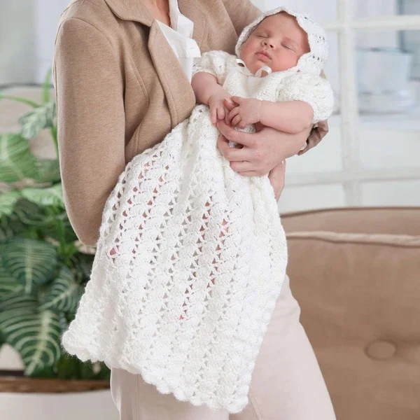 A woman holding a baby dressed i a long crochet christening dress and a crochet bonnet.