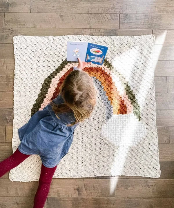 A young child playing on a crochet rainbow baby blanket.
