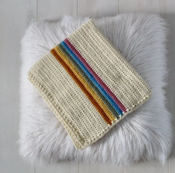 A white crochet baby blanket with a rainbow stripe.