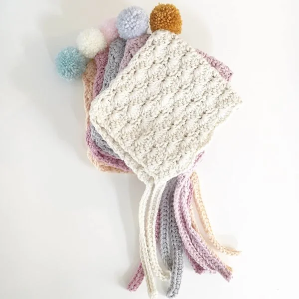 Astack of crochet baby bonnets with pompoms.