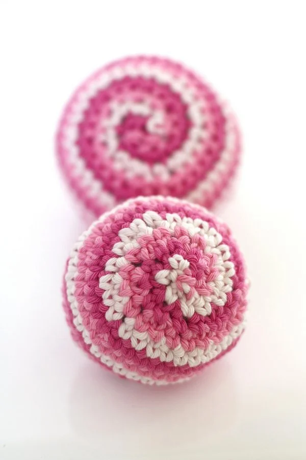 Two spiral crochet balls made in contrasting shades of pink.