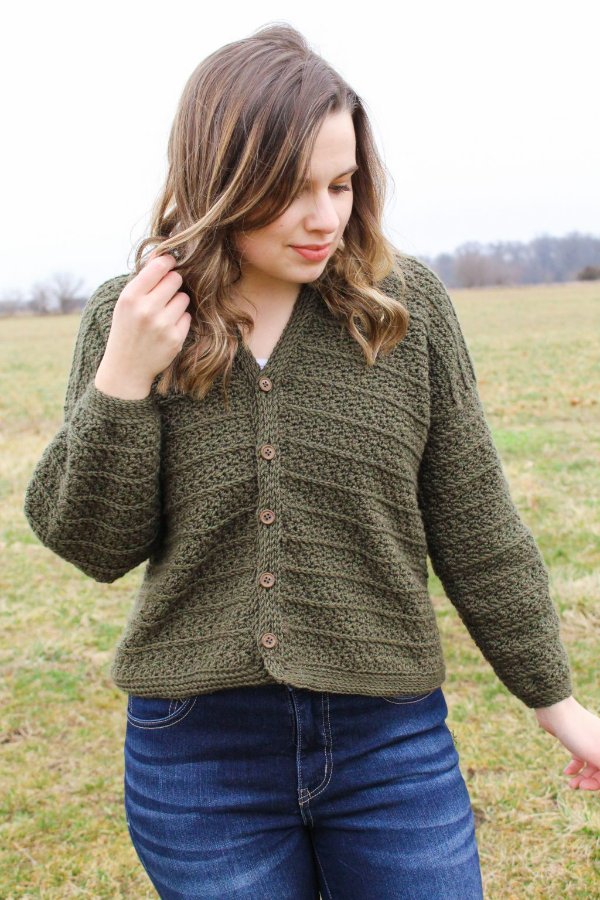 A close-up image of a woman wearing an olive green button-up crochet cardigan.