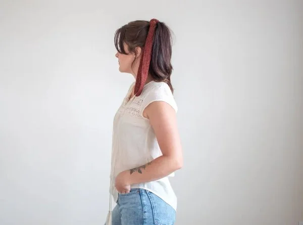 Side view of a woman wearing a rust coloured crochet hair tie with a ponytail.