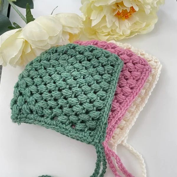 A stack of three different coloured crochet baby bonnets.