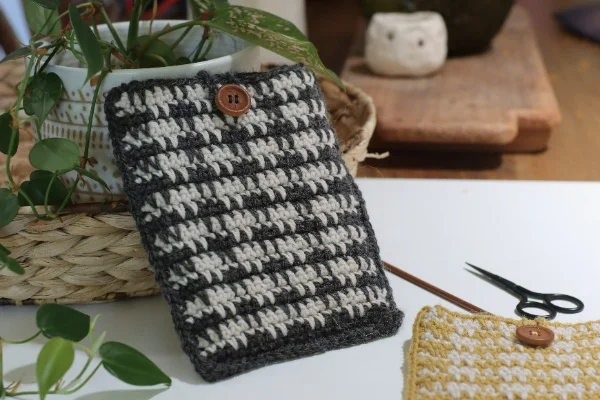 A black and white crocht kindle sleeve with crochet supplies and greenery.