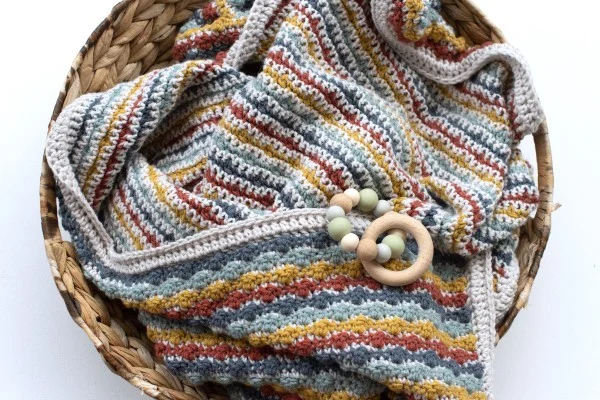 A closeup of a reversible crochet baby blanket in a basket.