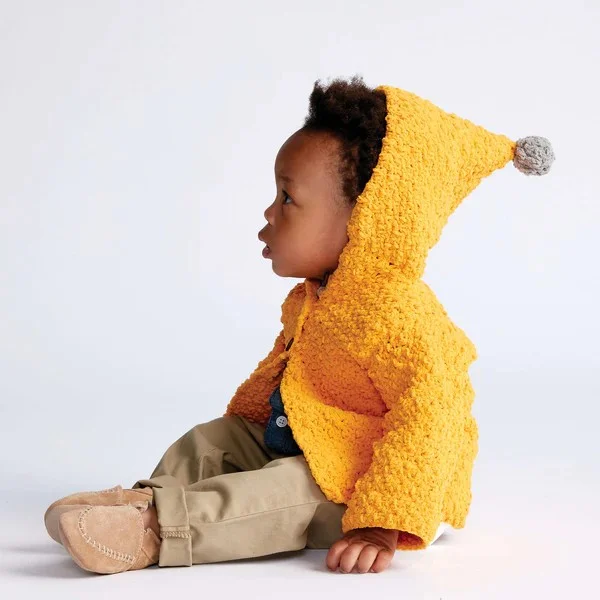 A baby wearing a yellow crocheted cardigan with a hood.