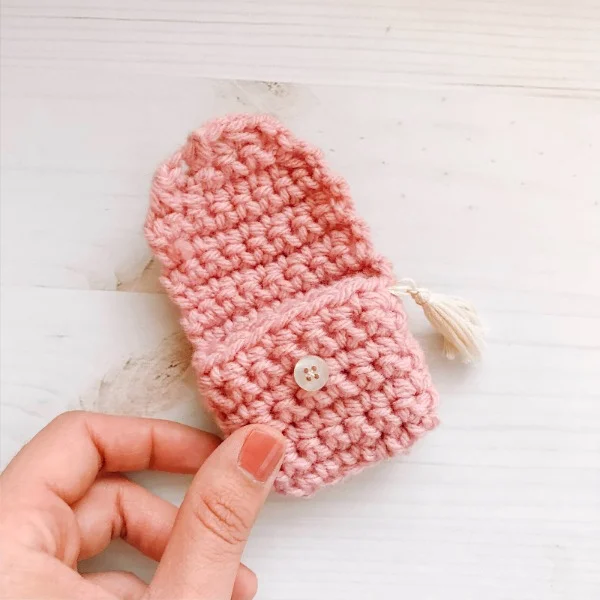 A pink crochet airpods case held in a hand.