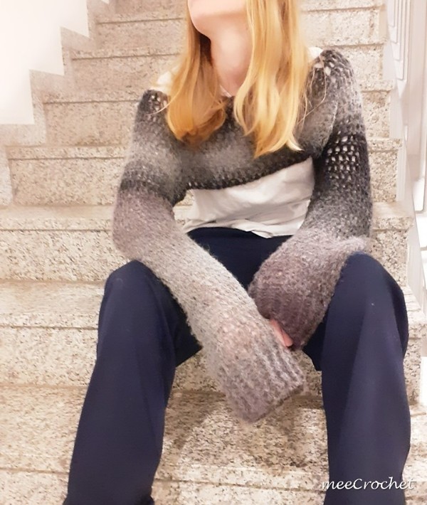 A woman sitting on steps wearing a crochet long sleeve crop top.