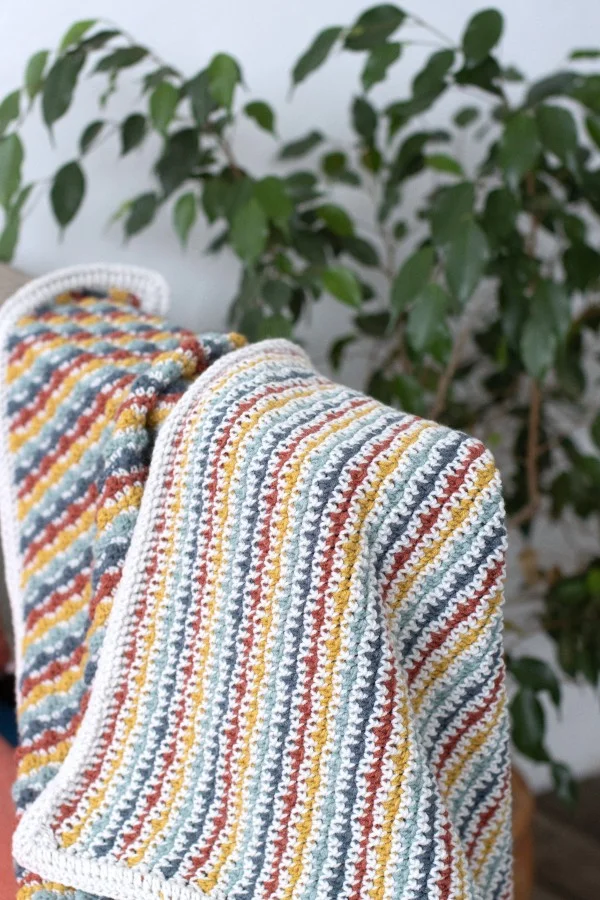 A reversible striped baby blanket haning to show both sides.