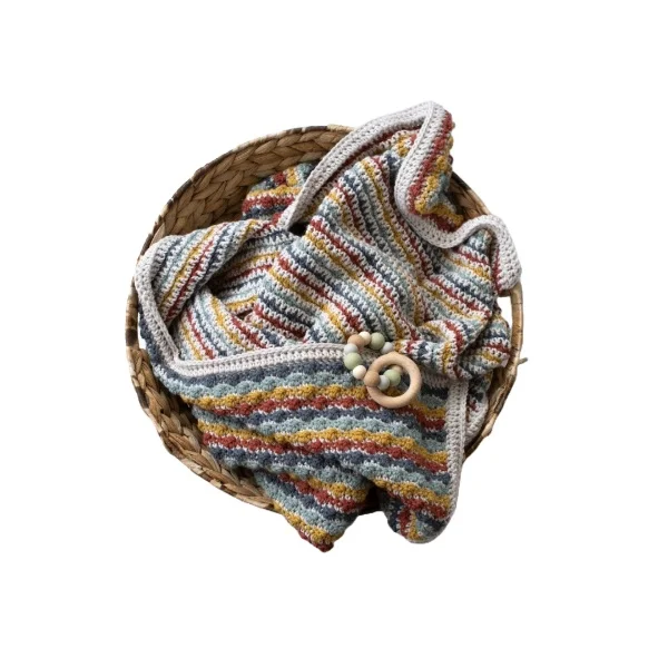 A striped, reversible crochet baby blanket in a bsket.