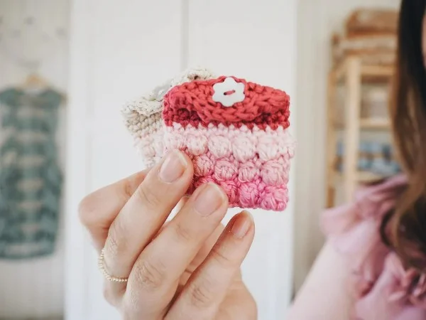 A tiny crochet earbud pouch in shades of pink and red.