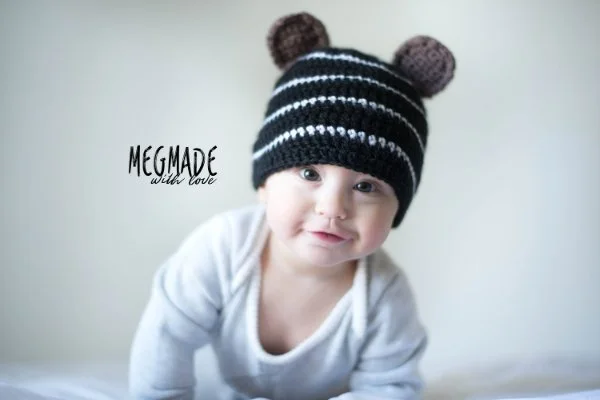 A baby wearing a striped baby bear cub crochet hat.