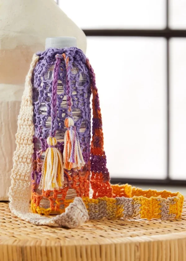 A boho-style crochet water bottle holder with a drawstring and tassels.