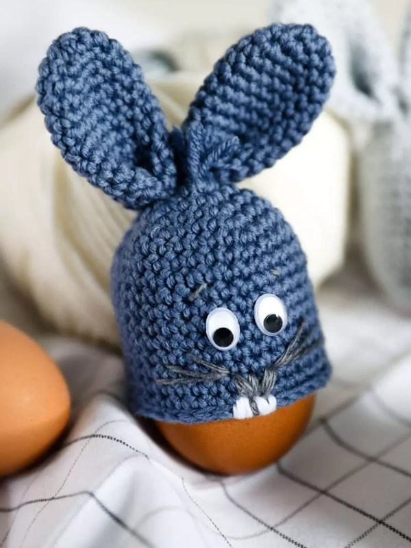 A crochet bunny egg cozy with wobbly eyes and embroidered whiskers and teeth.