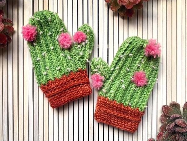 A flat-lay image of a pair of crochetd childs mittens with a cactus theme.